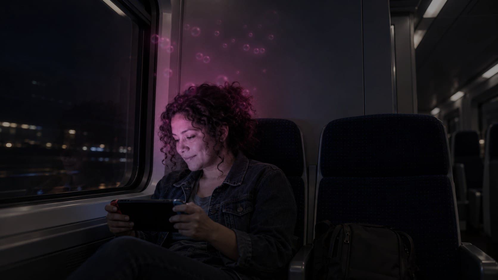 A woman playing a handheld game on a night train, soft pink bubbles rising from her curls and lighting the carriage wall.