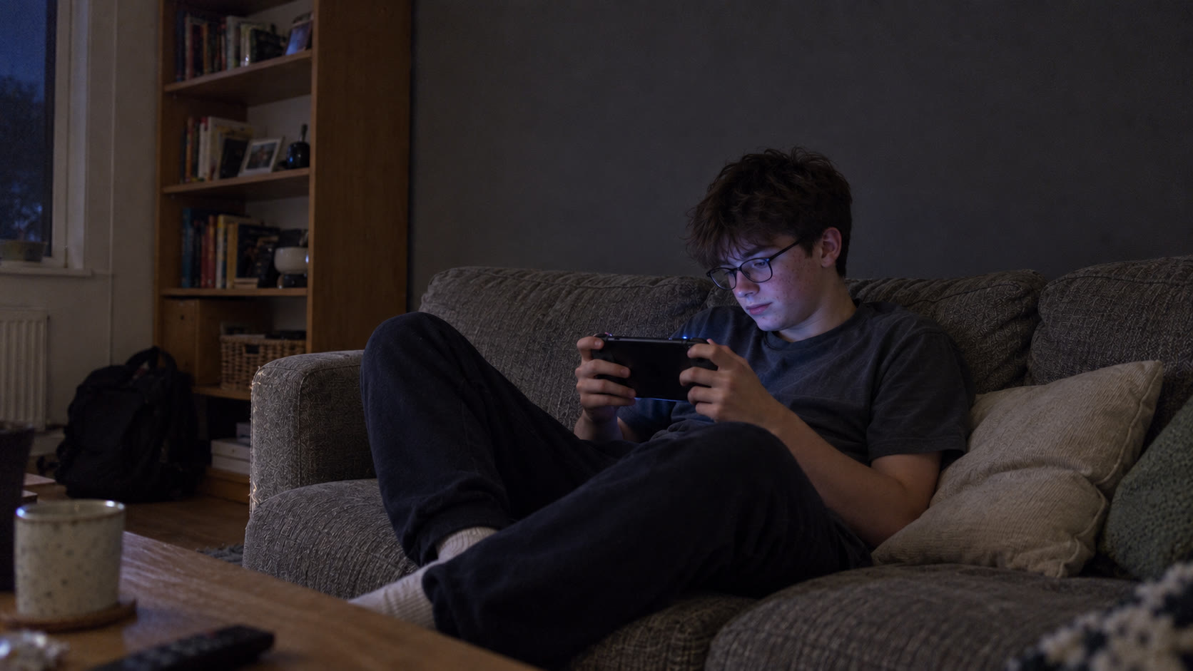 A teenage boy relaxing on a sofa with a handheld game, with animated pink bubbles forming in his hair.